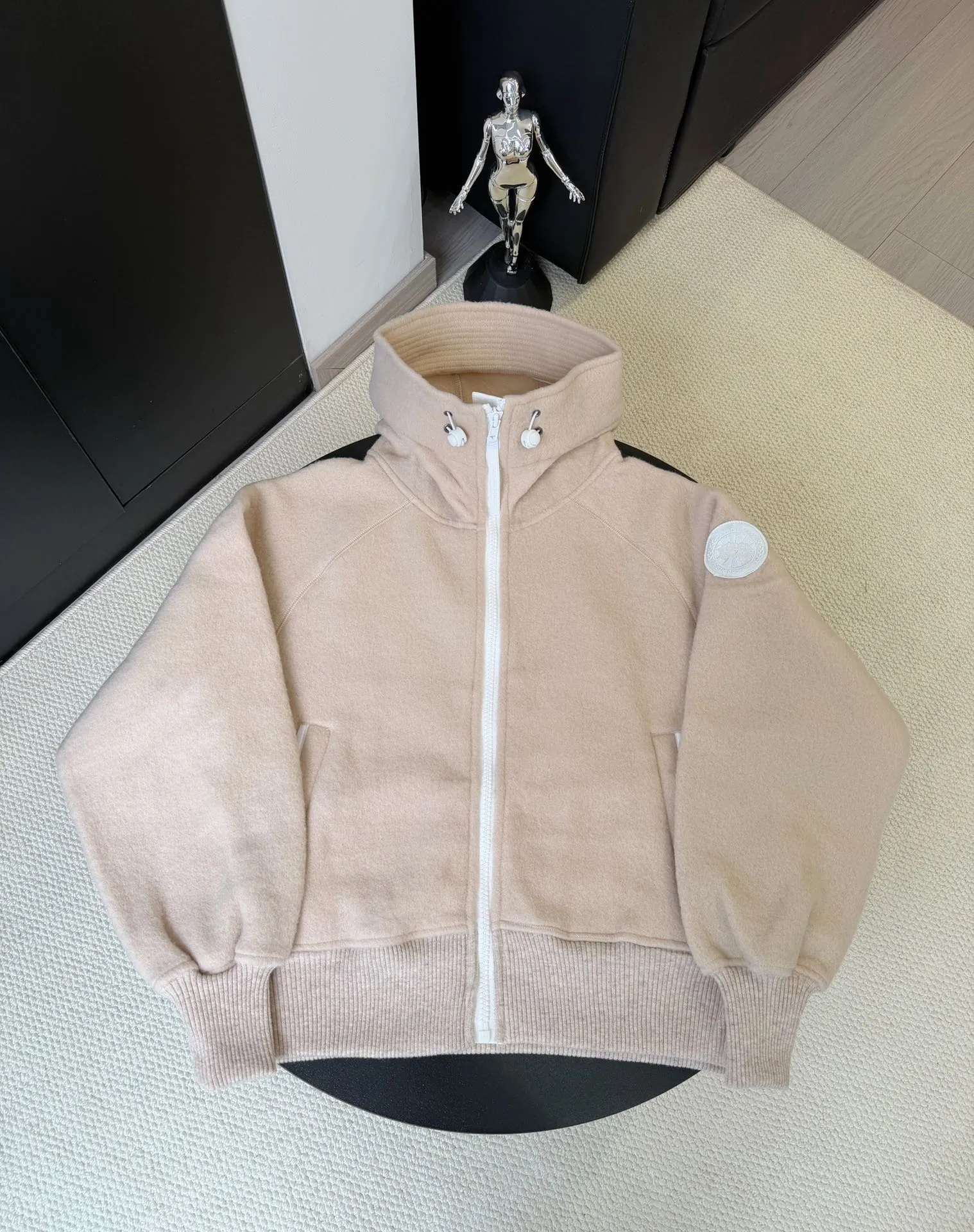 P660 Canada Goose Fleece Wool Badge Hooded Jacket Fabric selection: Wool fleece fabric blended with wool as the main body and a very small amount of spandex and polyester fiber. Wool is a core natural ingredient that provides unparalleled temperature regulation, antibacterial and anti-odor properties and a skin-friendly feel. The feeding of a small amount of spandex gives the fabric a certain degree of four-way elasticity, making it non-restrictive during daily activities. As the basis of fleece's structure, polyester fiber enhances the fabric's durability, wrinkle resistance and quick-drying properties. It contributes to the loft of the fleece and provides functions such as trapping air.  Detail 1: The sleeves and hem are closed with 2×2 ribbing. Its strong elasticity can closely fit wrists and waists of different thicknesses, forming an effective 'seal' to prevent cold wind from blowing back. It can still maintain its original shape after repeated stretching and use, and is not easy to loose and deform. And the ribbed cuffs can convey a sense of design and enhance the visual beauty.  Detail 2: The combination of hood design and elastic buckle improves warmth and windproof performance when wearing. Accessories: Customized elastic drawstring, elastic buckle, custom zipper pendant, custom armband Size: S M L Color: black gray coffee rice pink